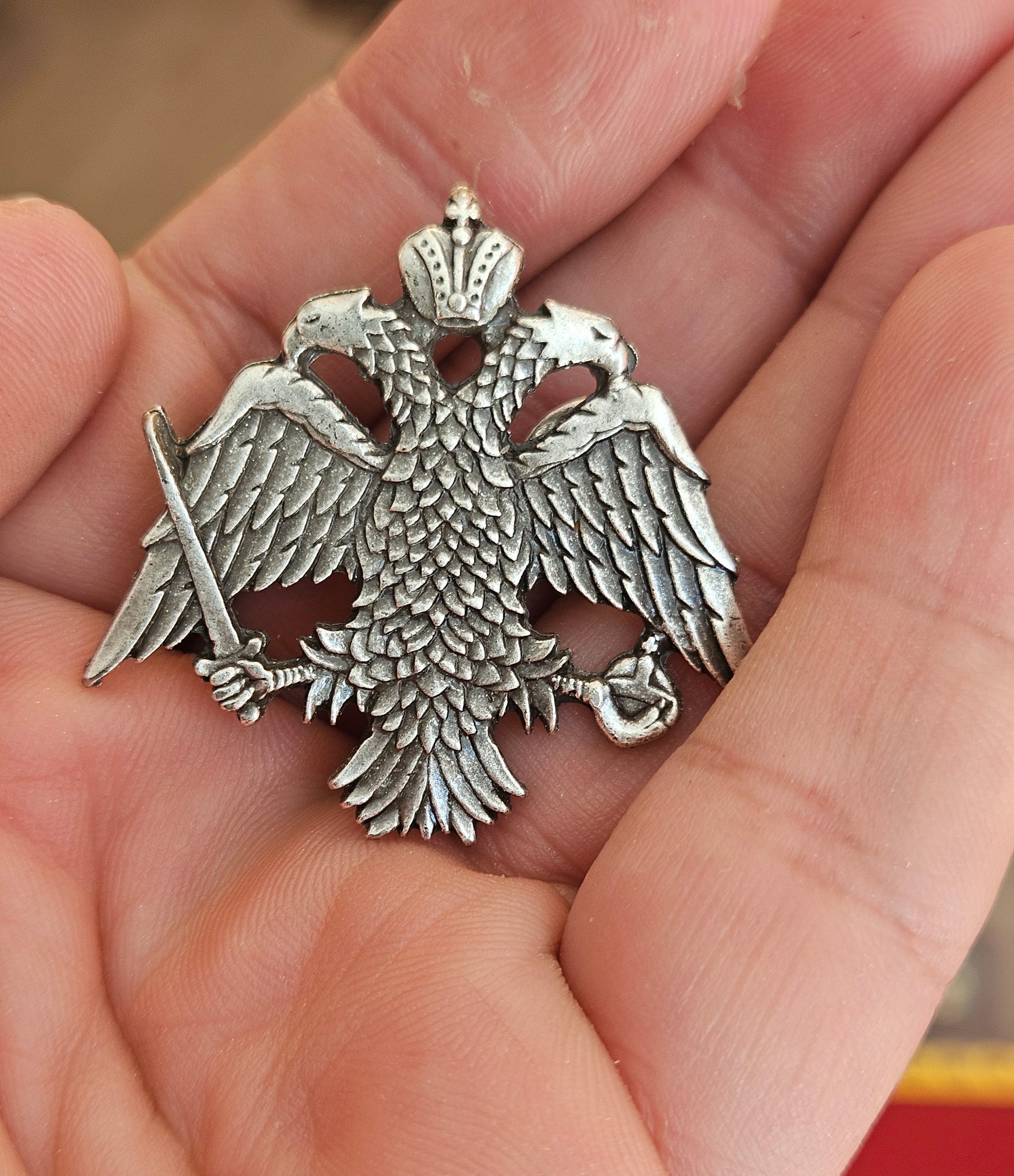 Large-scale handcrafted Orthodox double headed eagle crest lapel pin held on a hand for size reference