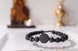 Black beaded bracelet on a white surface with blurred religious statue and candle in the background