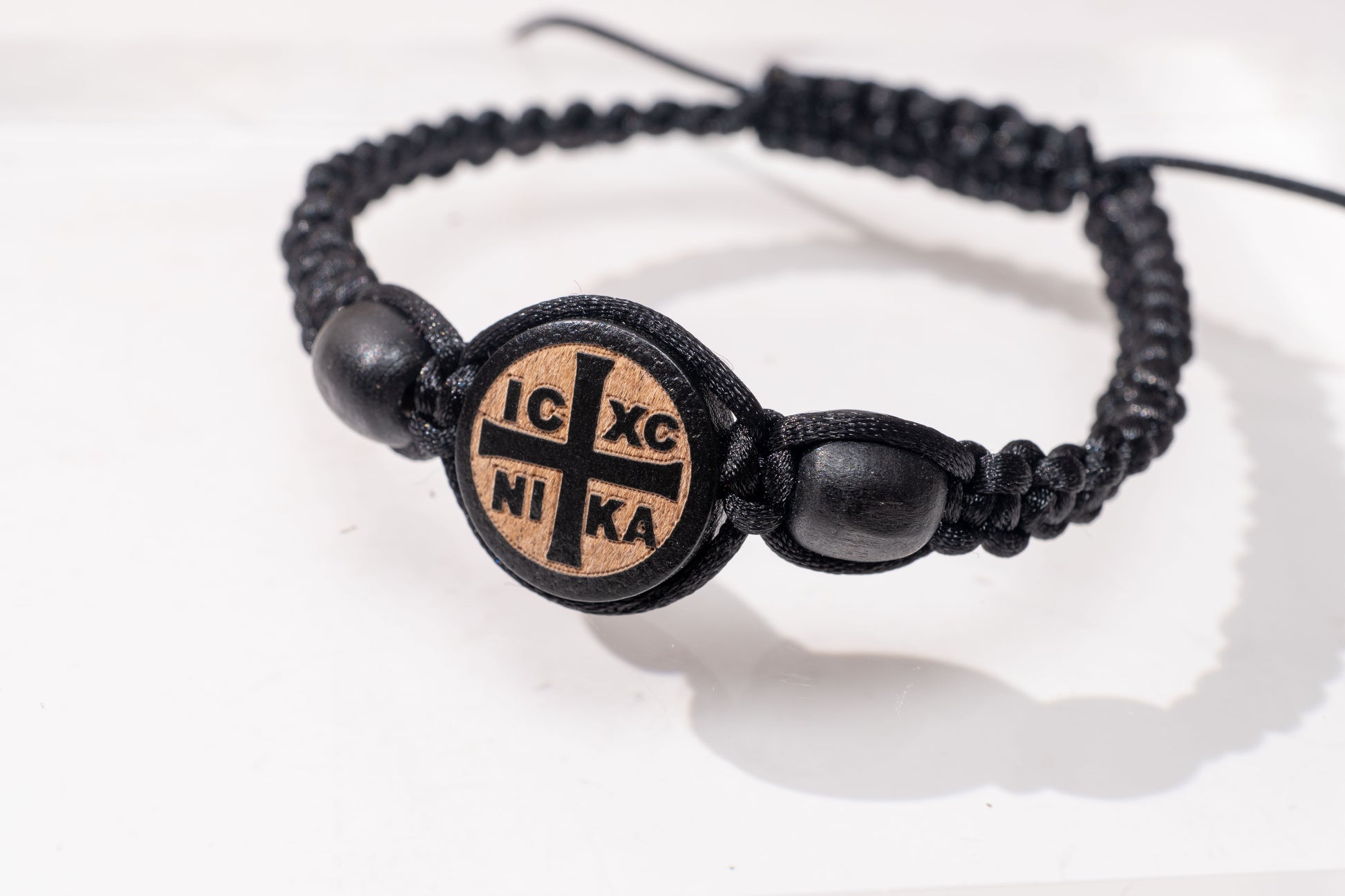 Ultra close-up view of the handcrafted black macrame Komboskini bracelet featuring an engraved round IC XC NIKA wooden cross