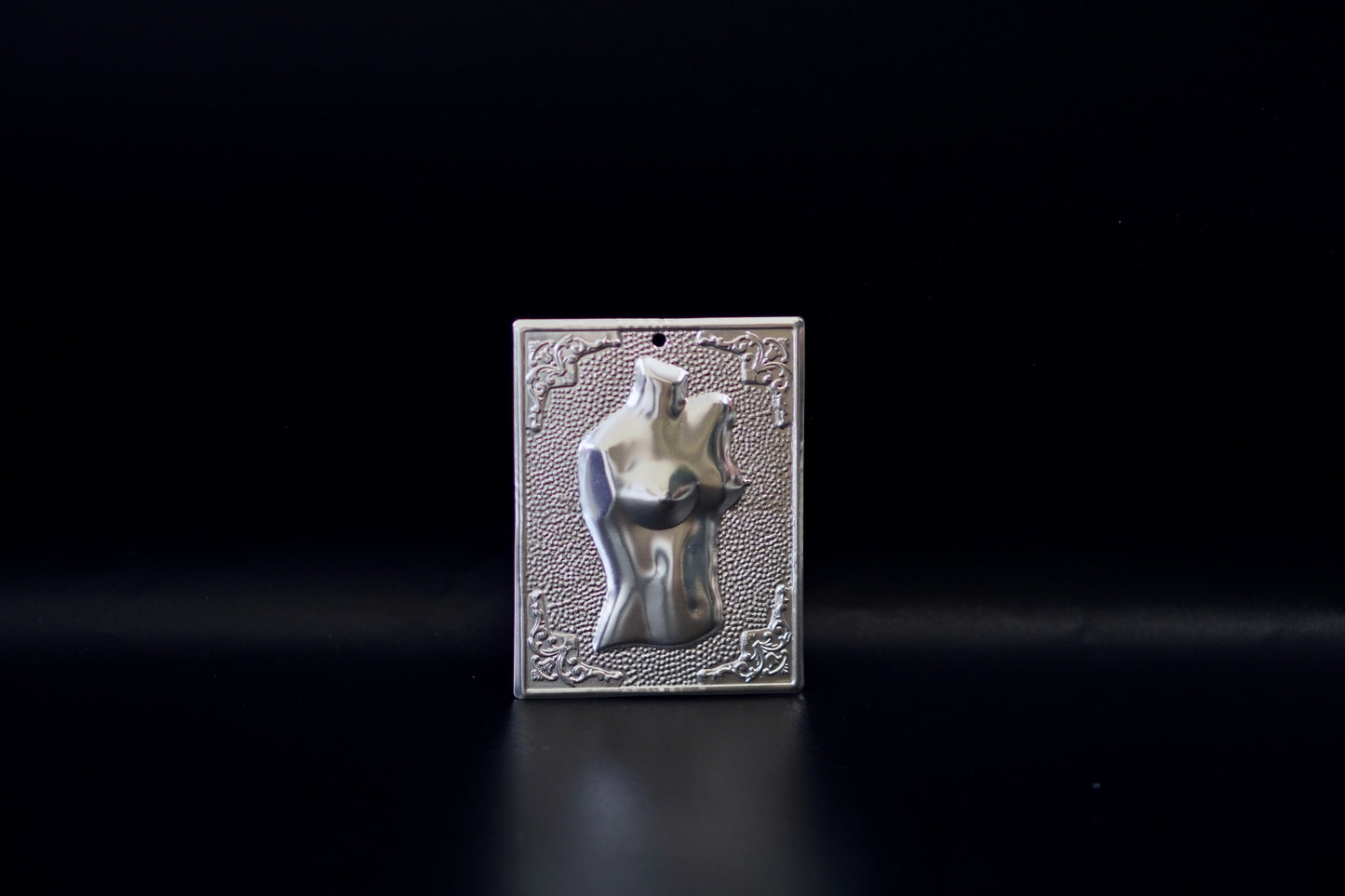 Plain silver-tone Greek Orthodox tama votive offering plaque embossed with a female torso motif and a small pre-drilled top hole for hanging.