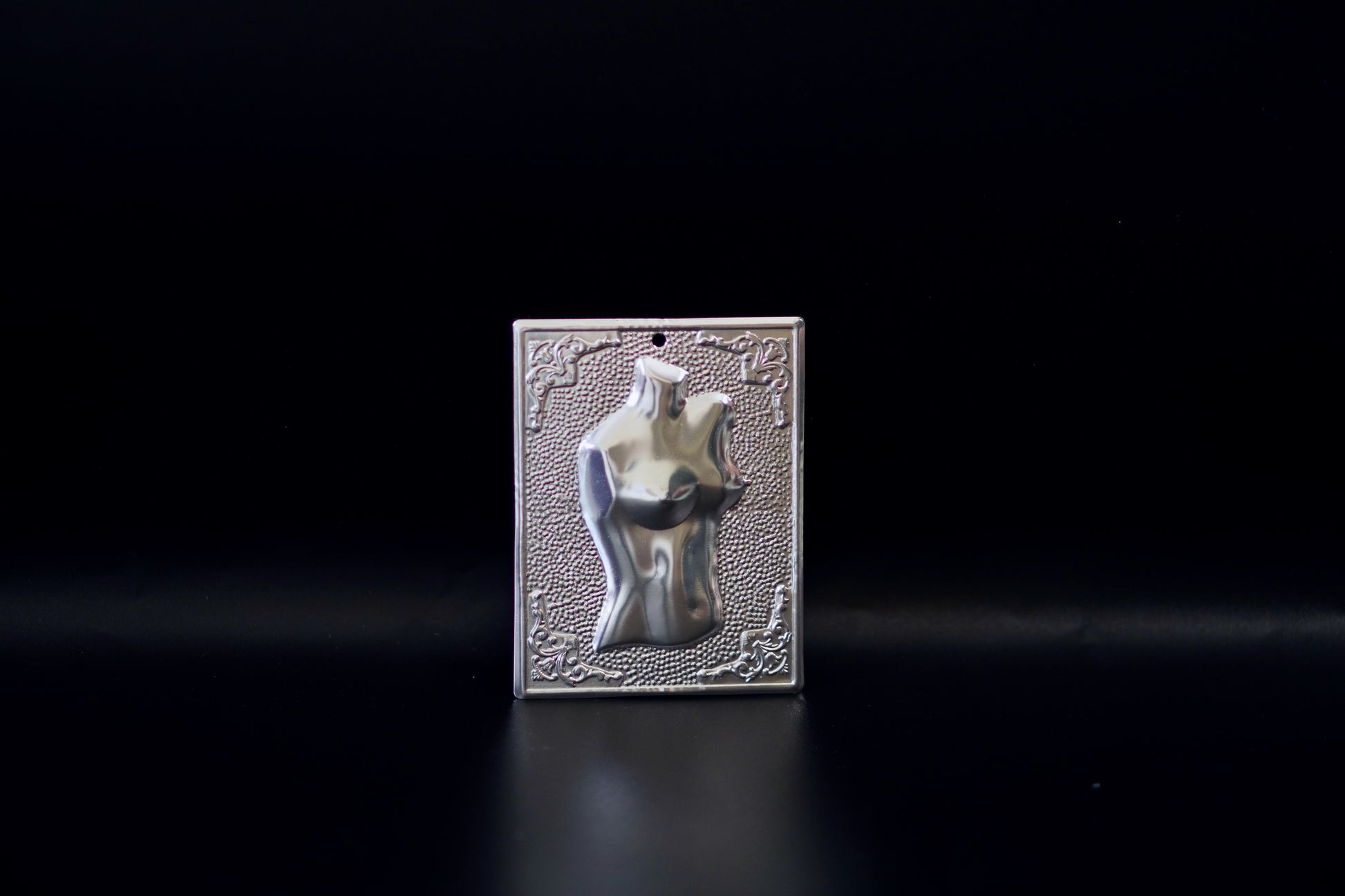 Plain silver-tone Greek Orthodox tama votive offering plaque embossed with a female torso motif and a small pre-drilled top hole for hanging.