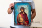 erson holding a religious icon of a bearded figure with a halo and cross.