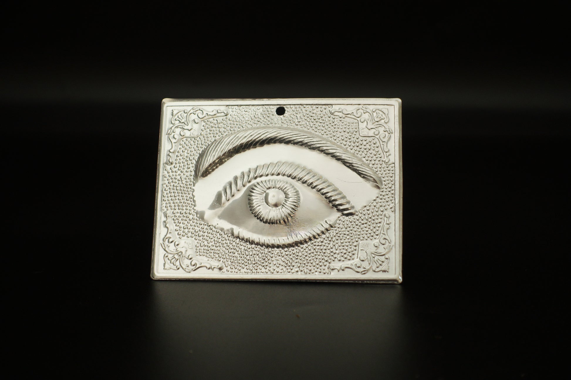 Plain silver-tone Greek Orthodox tama votive offering plaque embossed with a single eye motif and a small pre-drilled top hole for hanging.