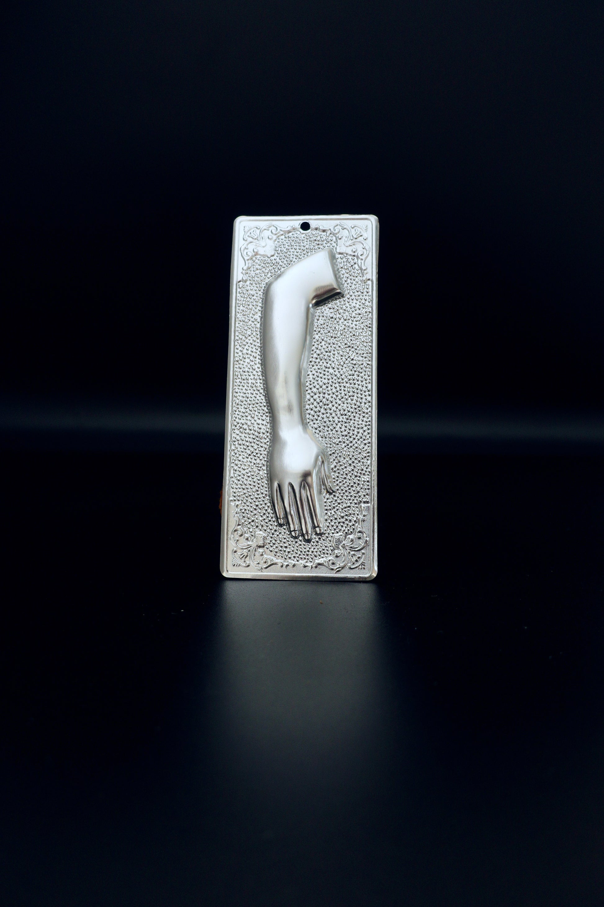 Plain silver-tone Greek Orthodox tama votive offering plaque embossed with a left human arm and hand design and a small pre-drilled top hole for hanging.