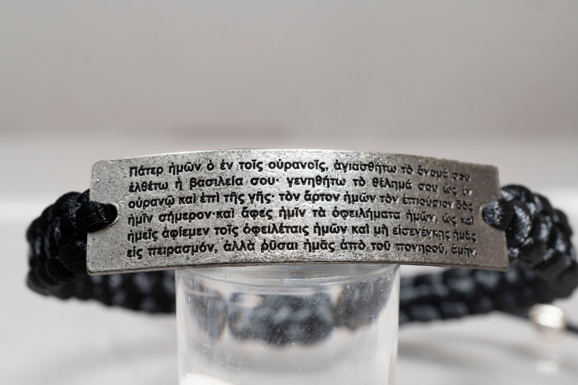 Detailed close up of the Lord's Prayer in Greek engraved on an antique silver plate macrame bracelet
