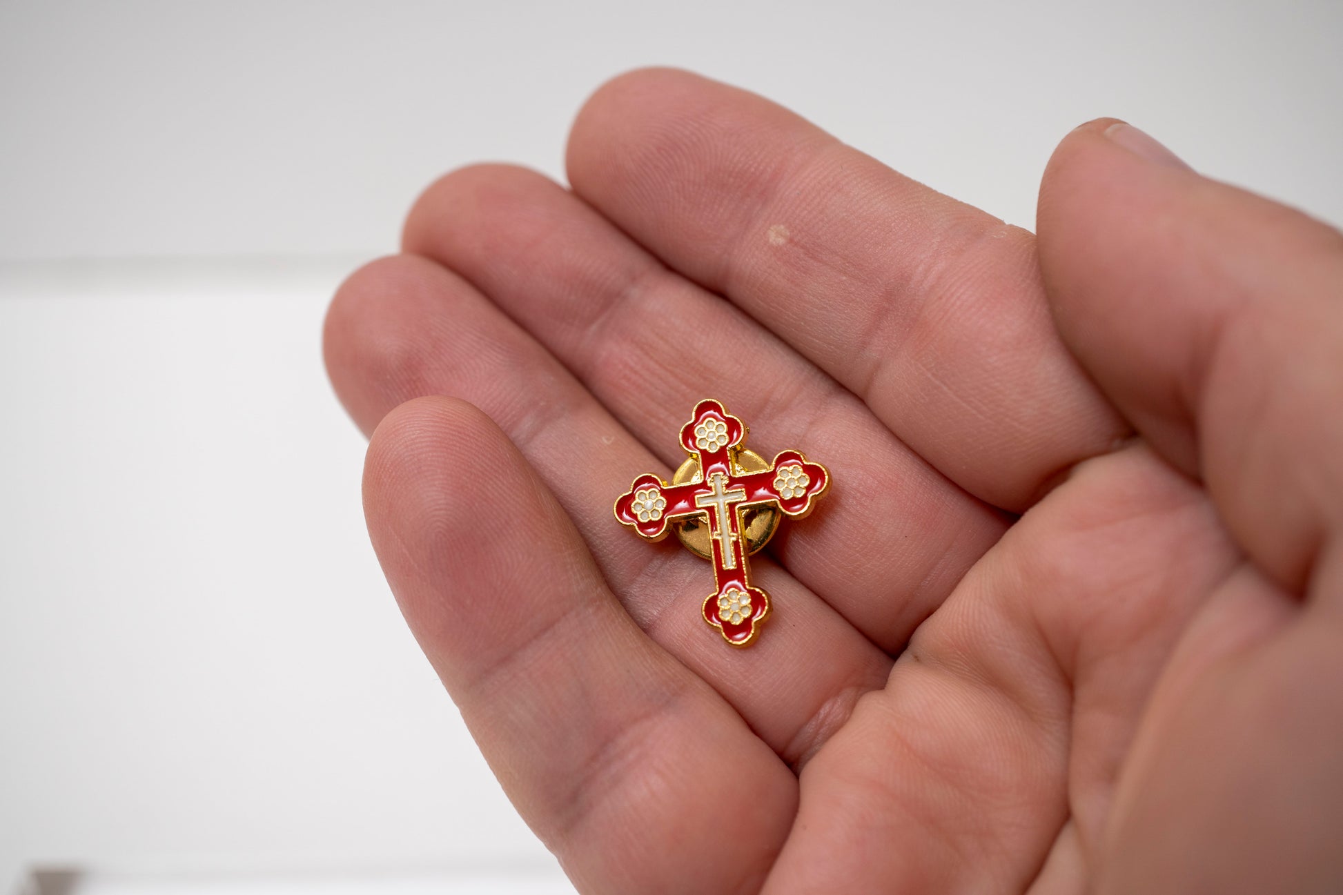 Rich red enamel Byzantine style cross lapel badge on a polished gold background