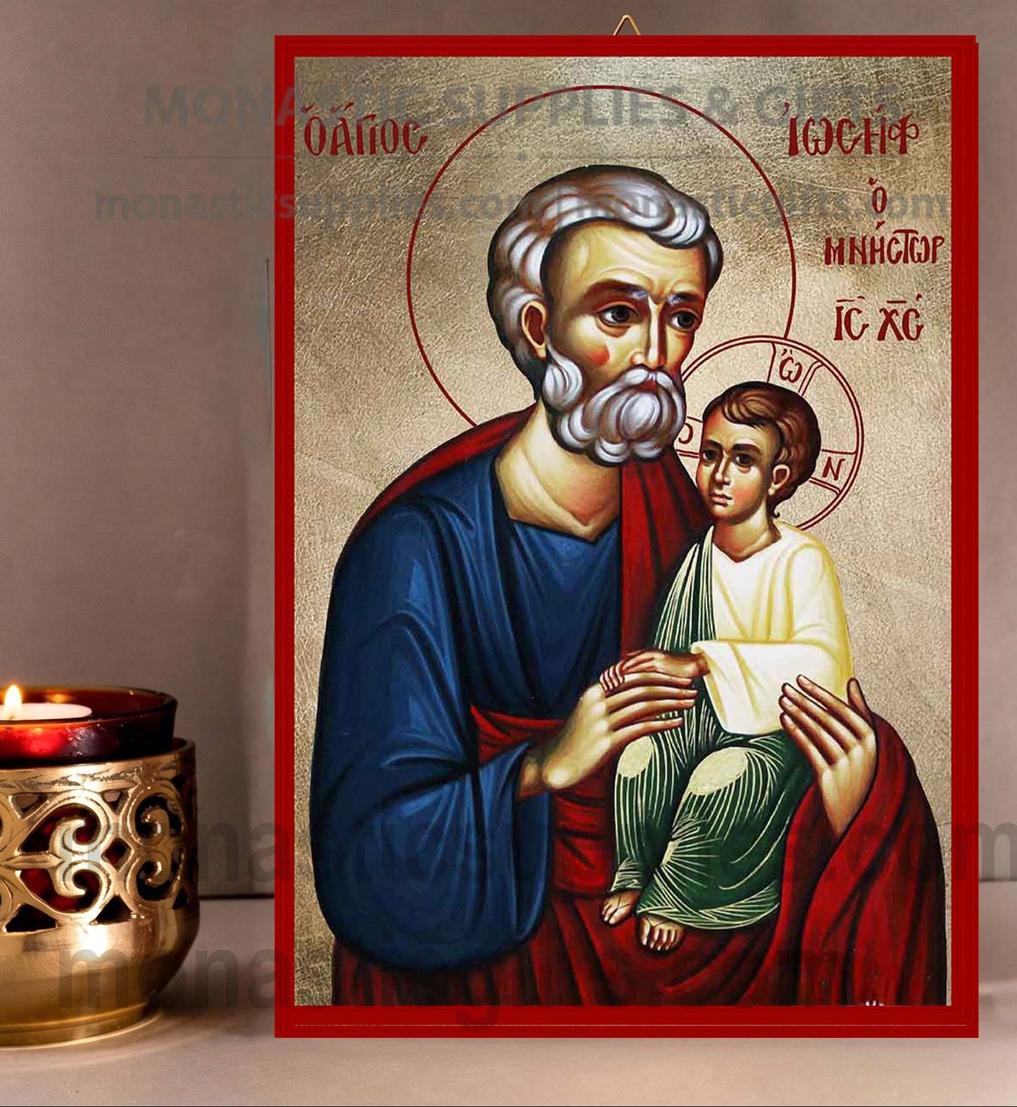 A religious icon plaque of Saint Joseph holding the infant Jesus, displayed on a neutral surface next to a lit brass candle holder.