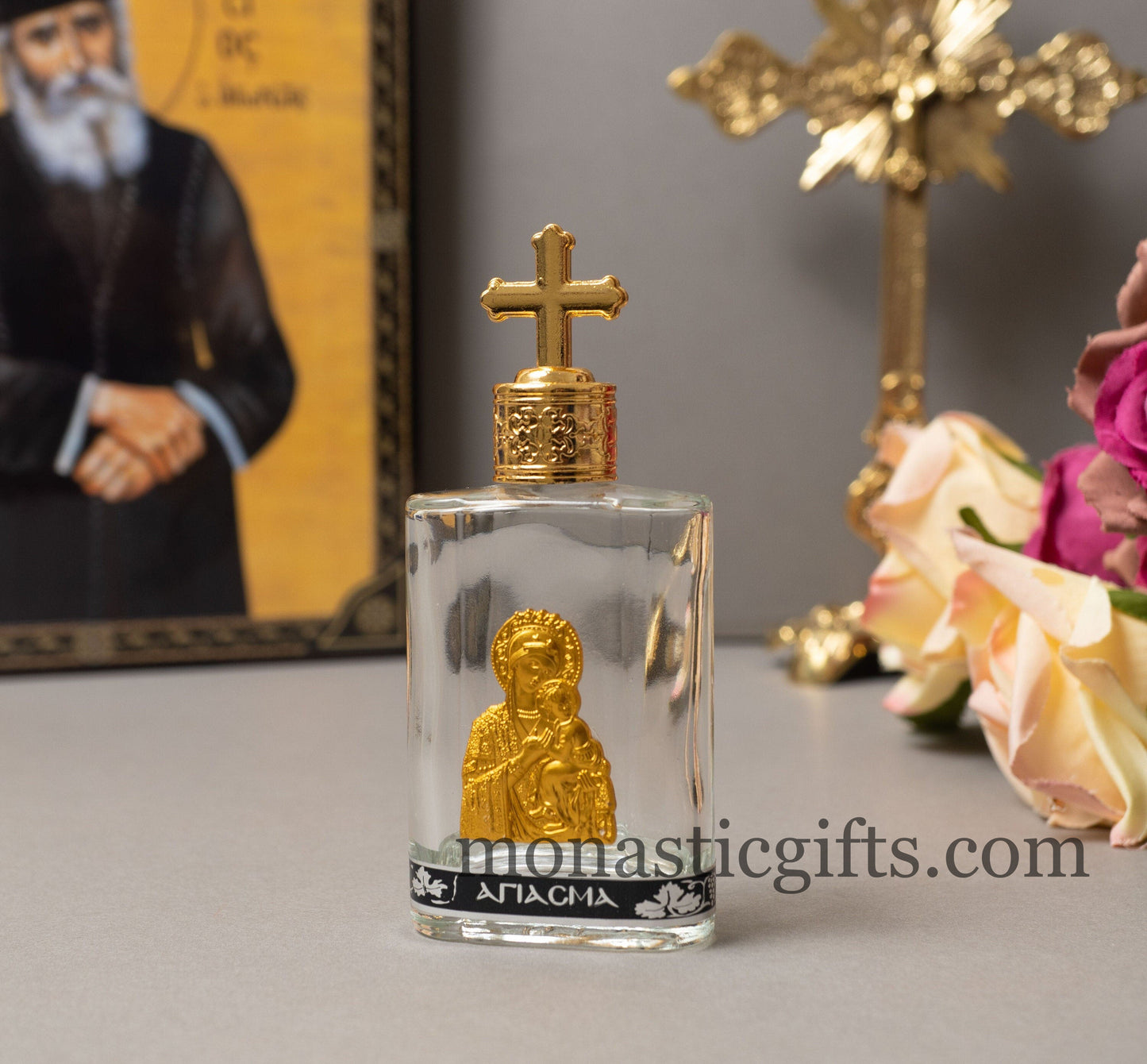 Glass holy water bottle with rounded corners featuring a gold-tone metal icon of the Theotokos and a matching screw cap with a cross, measuring 12x5x2 cm.